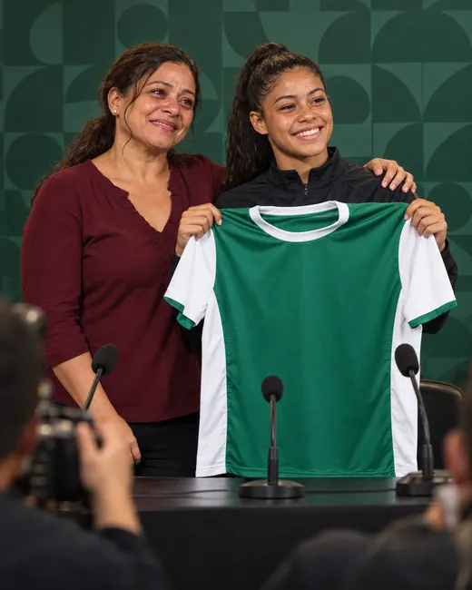 A mesma mãe, anos depois, ao lado da filha numa coletiva de imprensa de um clube, as duas sorrindo